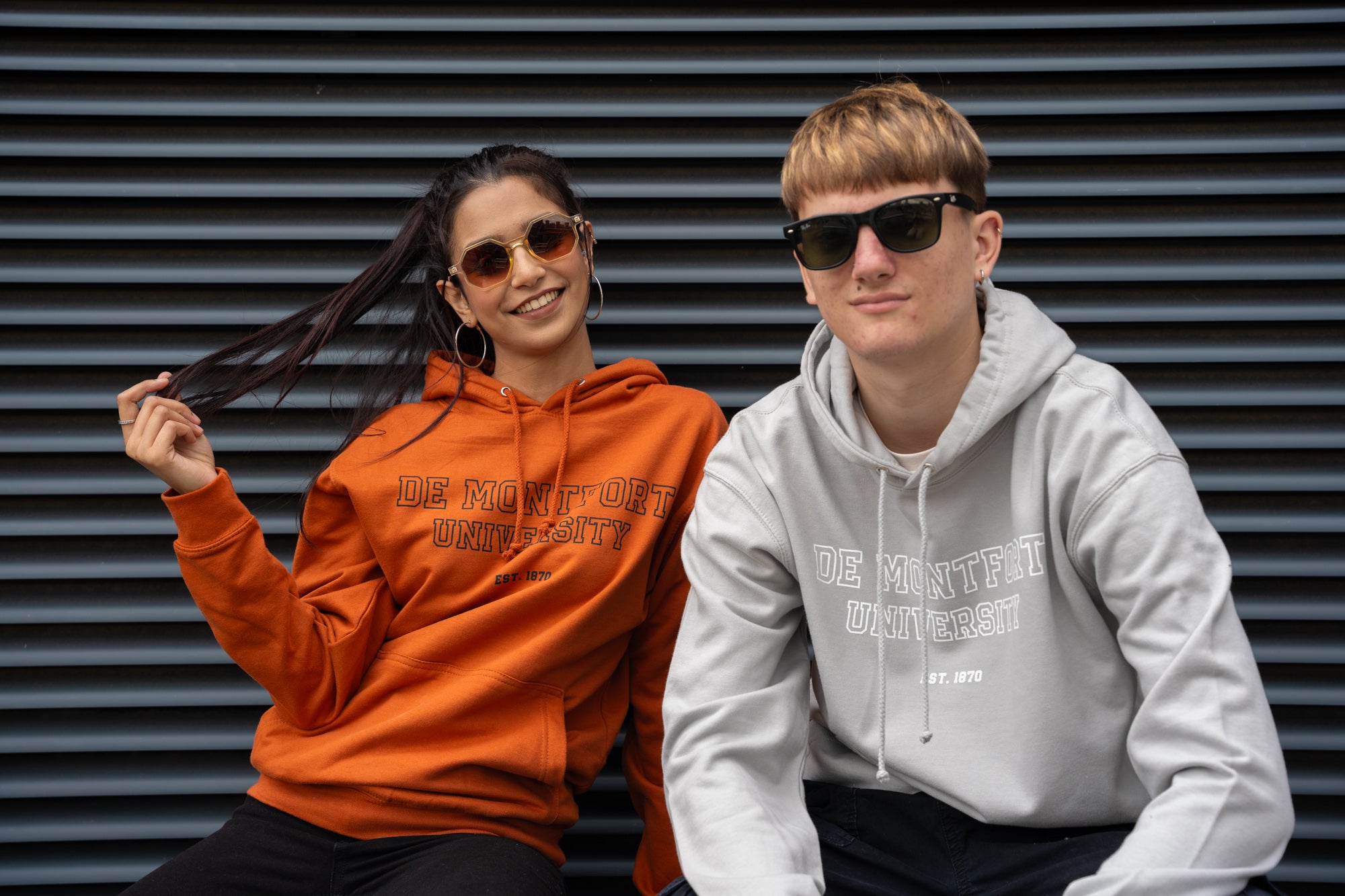 Two people wearing hoodies with text in front of a metallic background.